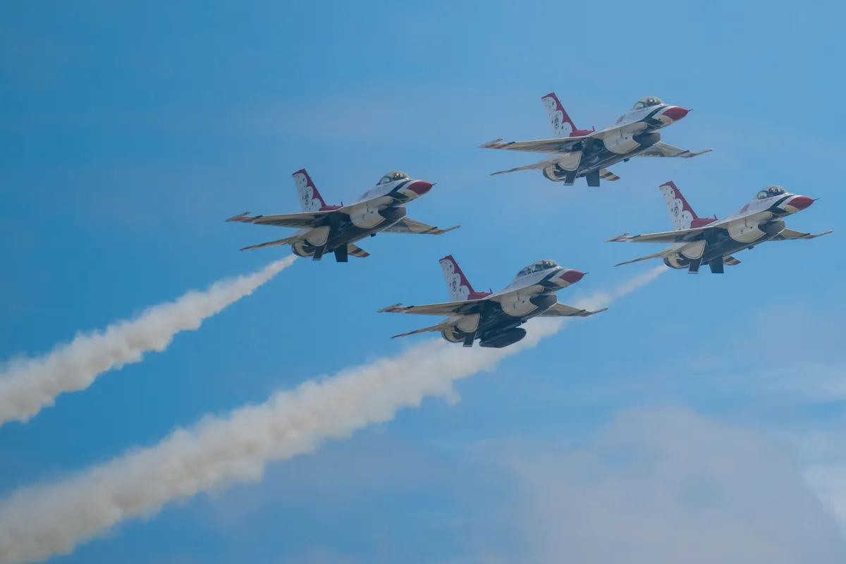 Four U.S. Air Force Thunderbirds F-16 Fighting Falcons banking in diamond formation against a clear sky, two of them trailing white smoke.